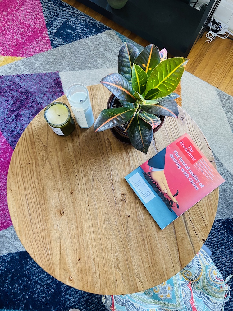 Bohemian coffee table with a plant, magazine, and candles and a colorful rug underneath 